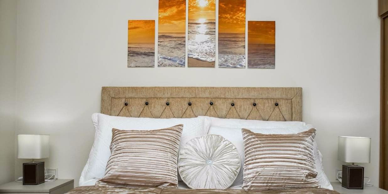 A bed with a wooden headboard, two bedside tables with lamps, and a sunset painting above.