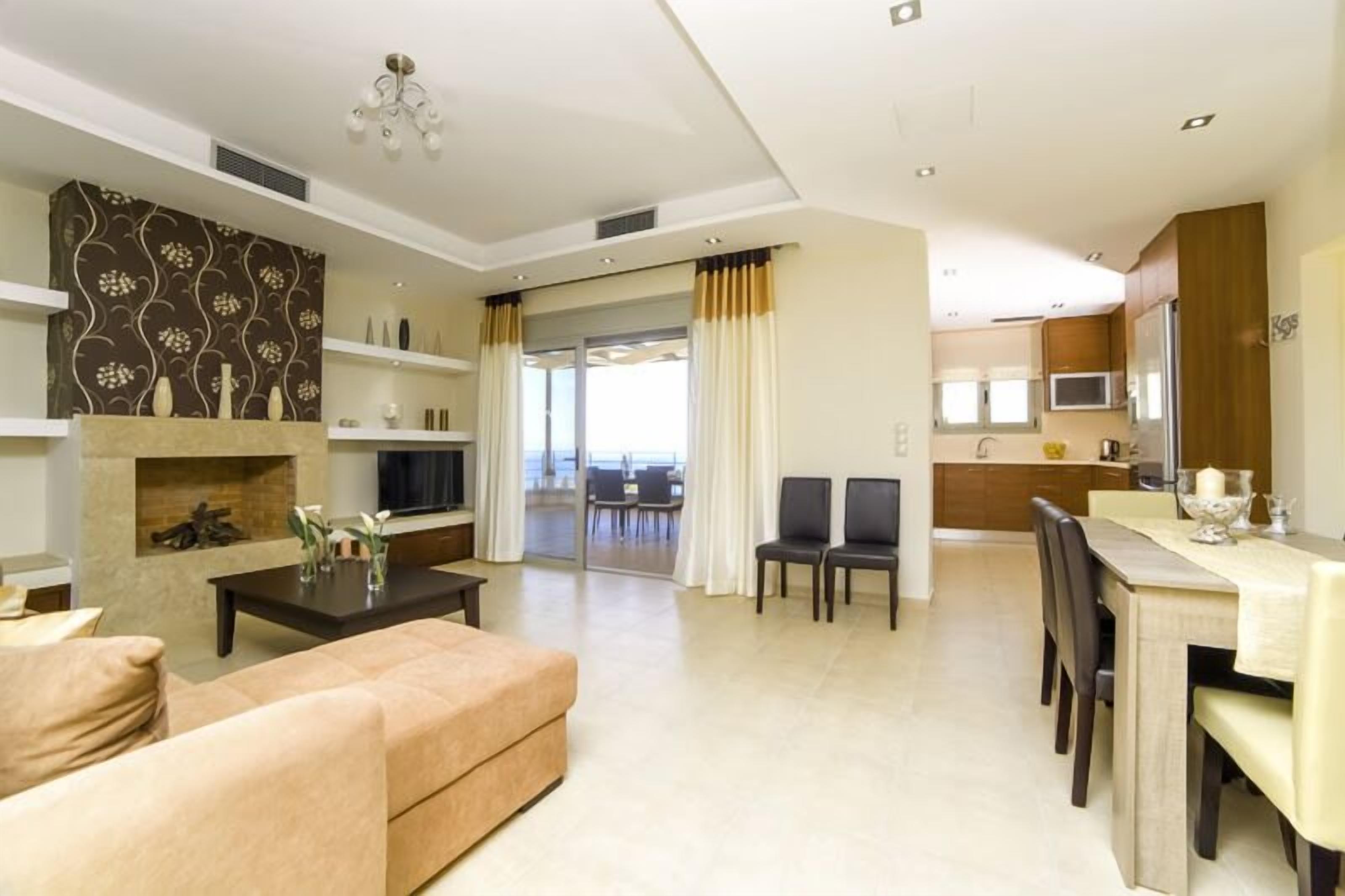 A modern living room with a fireplace, a dining area with a table and chairs, and a kitchen area with cabinets and a microwave.