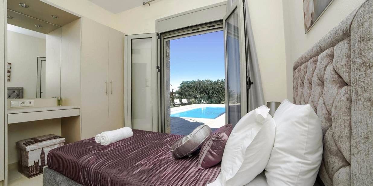 A bedroom with a bed, a bathroom with a mirror, and a view of a swimming pool.