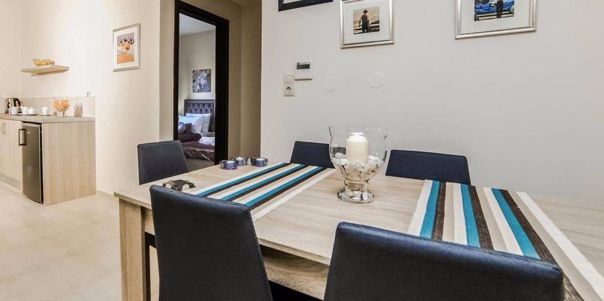 A dining area with a long table, chairs, and a kitchen in the background.