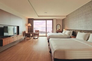 A hotel room with two beds, a TV, a desk, and a view of the outdoors.