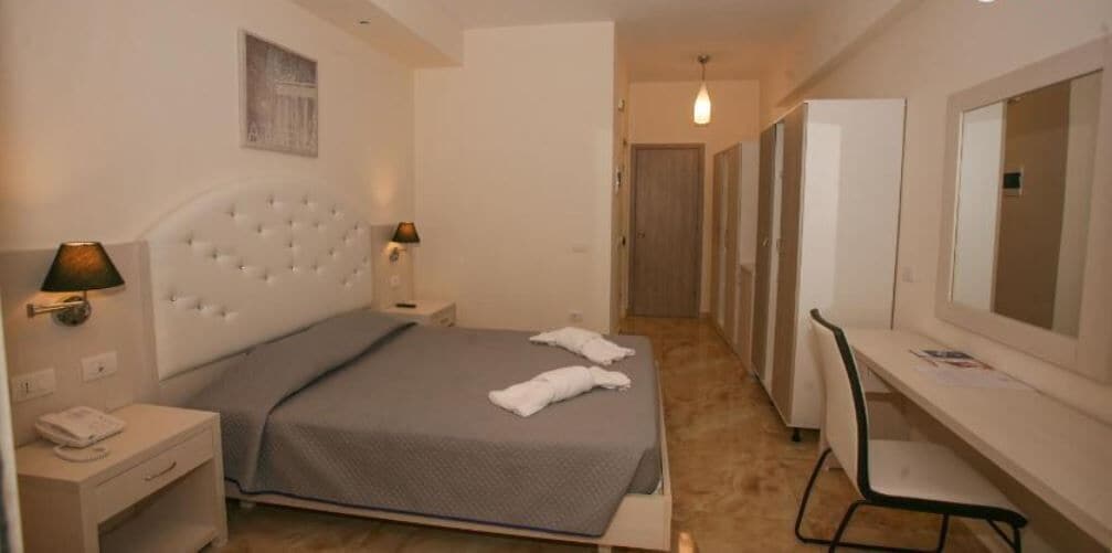 A hotel room with a bed, bedside tables, a desk, and a chair.