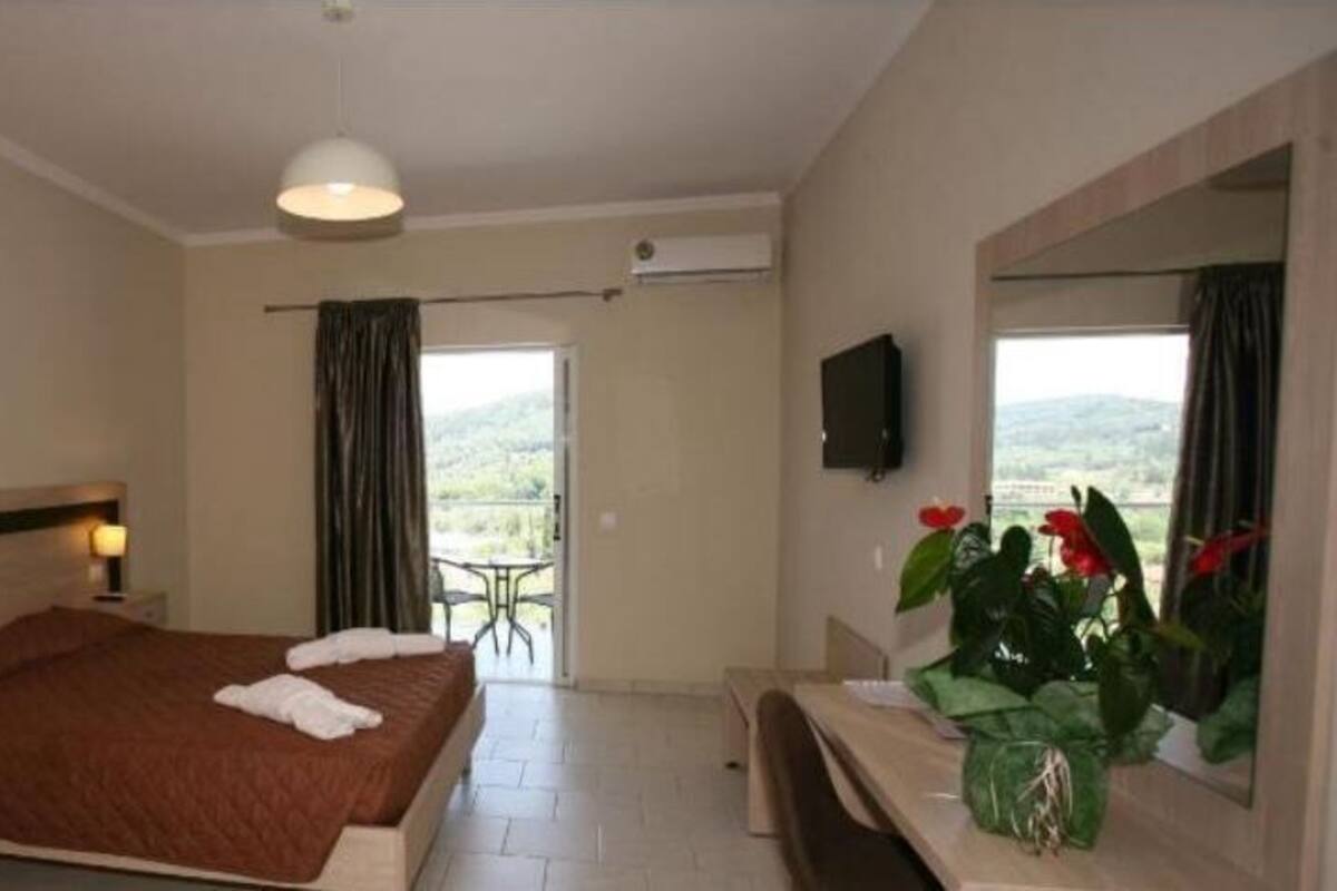 A hotel room with a bed, bedside table, TV, and a view of the outdoors.