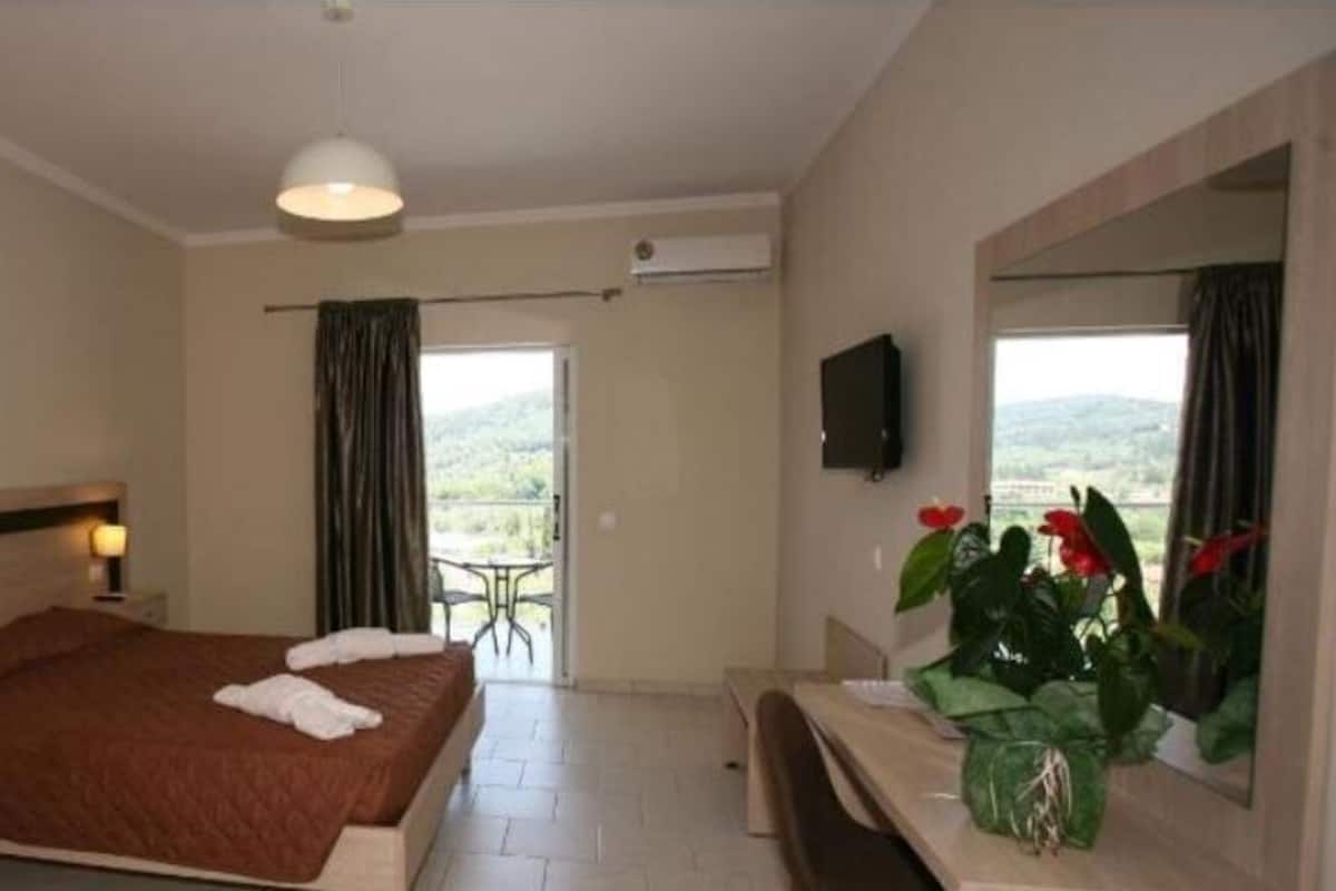A hotel room with a bed, bedside table, TV, and a view of the outdoors.