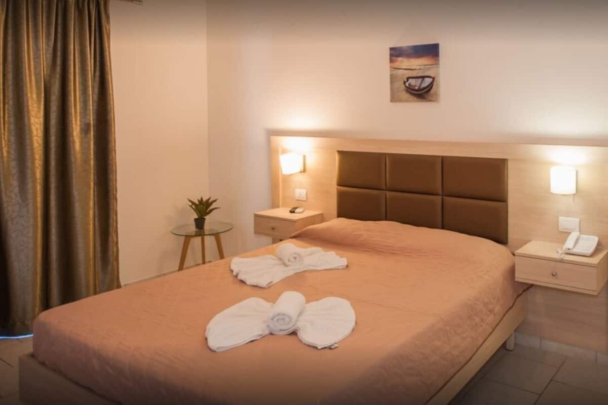 A hotel room with a large bed, two bedside tables with lamps, a small table with a plant, and a painting on the wall.