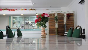 Taula de dinar amb un ram de flors, cadires verdes i una taula amb sobre de vidre en un interior modern amb cuina al fons.