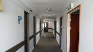 Passadís llarg i estret amb portes a ambdós costats, un extintor a la paret dreta i un senyal que indica la direcció de l'ascensor.