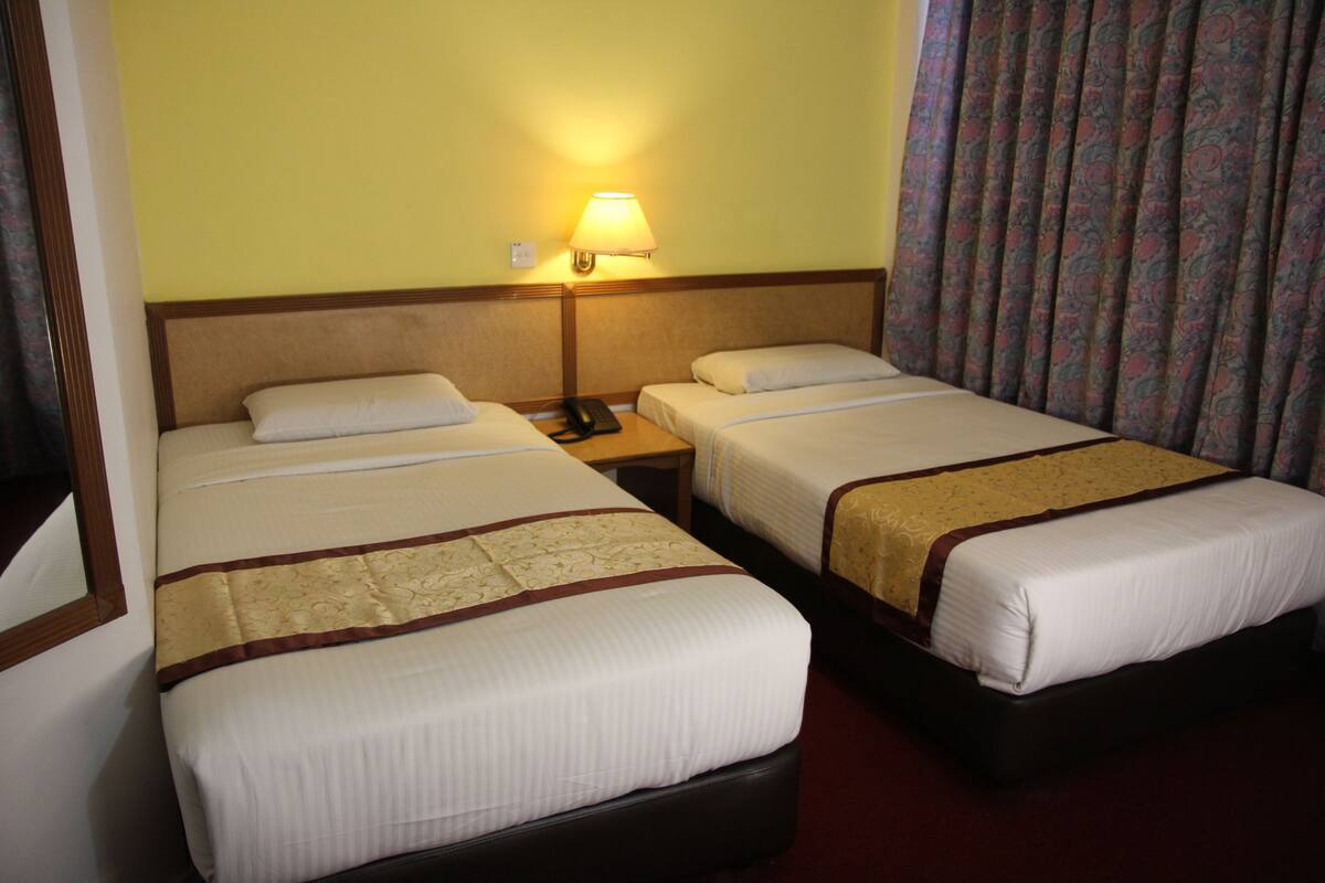 Una habitación de hotel con dos camas individuales, una mesita de noche con lámpara y una cortina estampada.