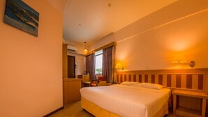 A hotel room with a large bed, a desk, a chair, a lamp, and a painting on the wall. - Miri Hotel (Miri)