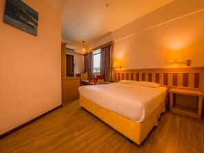 Una habitación de hotel con una cama grande, un escritorio, una silla, una lámpara y un cuadro en la pared.