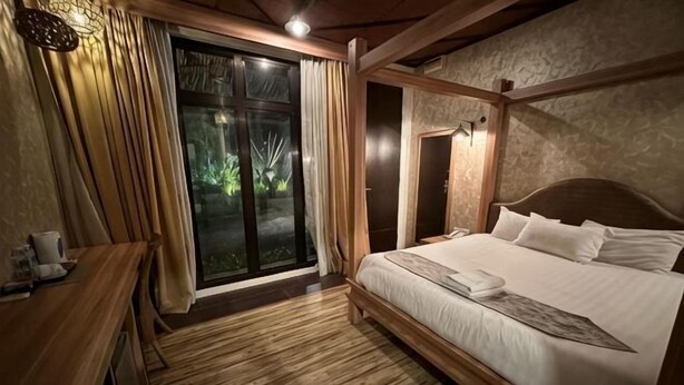 Un dormitorio con cama de madera, un escritorio y un ventanal corredera que da a un balcón.
