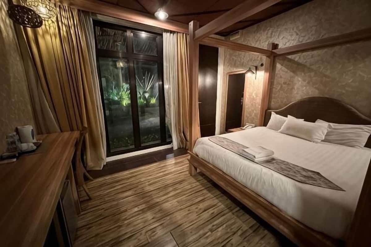 A bedroom with a wooden bed, a desk, and a sliding glass door leading to a balcony.