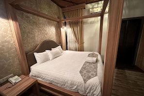 Quarto com uma cama grande, cabeceira de madeira, telefone ao lado da cama e almofada decorativa estampada.