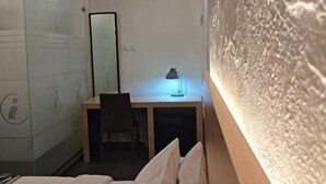 Habitación de hotel con cama, escritorio, silla, lámpara de escritorio y espejo en la pared.