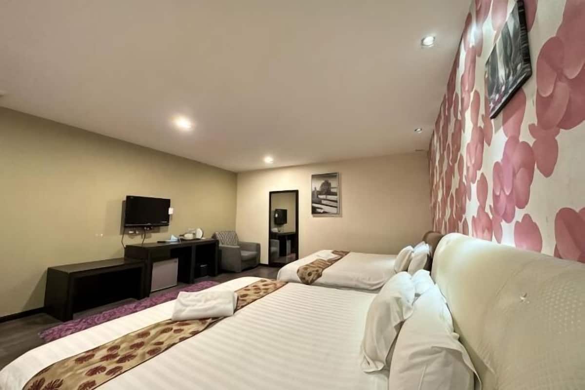 A hotel room with two beds, a desk, a chair, a TV, and a wall with a floral pattern.