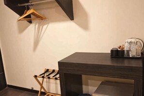 A room with a dark wooden table, a hanging clothes rack, and a small shelf with a kettle and cups. - I Garden Hotel (Ipoh)