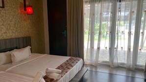 Una habitación de hotel con una cama grande, un cabecero, una puerta y vistas a través de cortinas translúcidas.