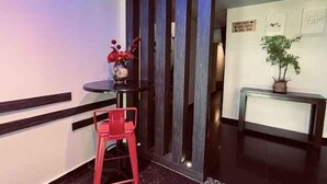 A reception area with a reception desk, a red chair, a vase with flowers, and a potted plant. - I Garden Hotel (Ipoh)