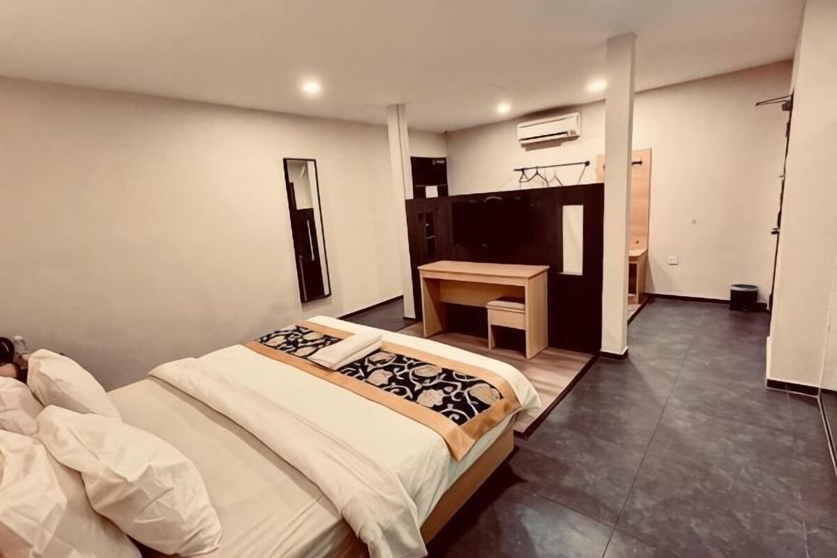 A modern hotel room with a large bed, a desk, a mirror, and a wardrobe.