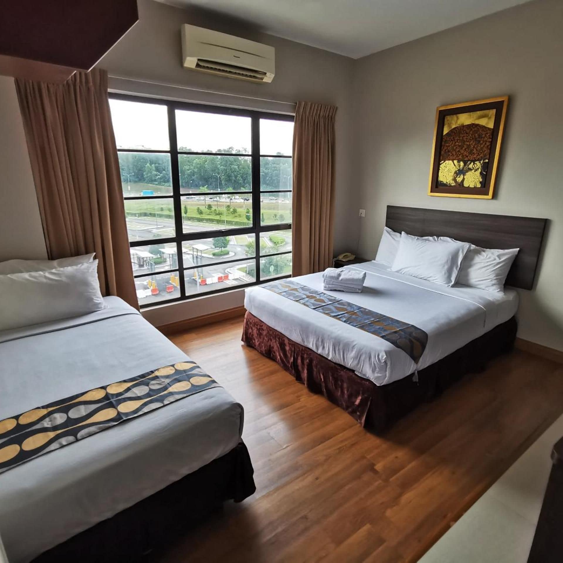 A hotel room with two beds, a large window with a view, an air conditioning unit, and a framed picture on the wall.