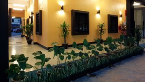 Un couloir aux murs jaunes, agrémenté de plantes en pot et de luminaires fixés au mur.