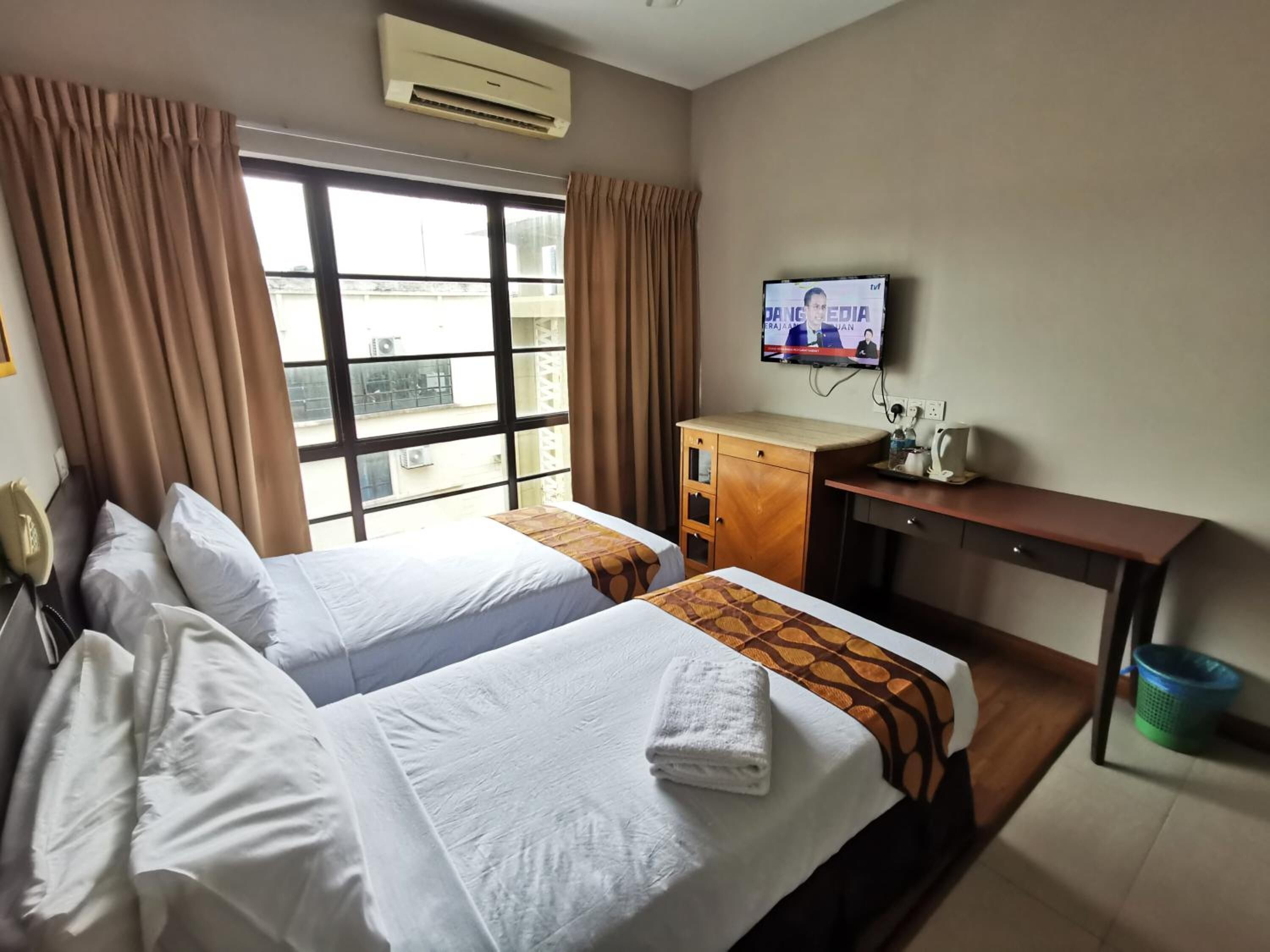 A hotel room with two beds, a TV, a desk, and an air conditioning unit.