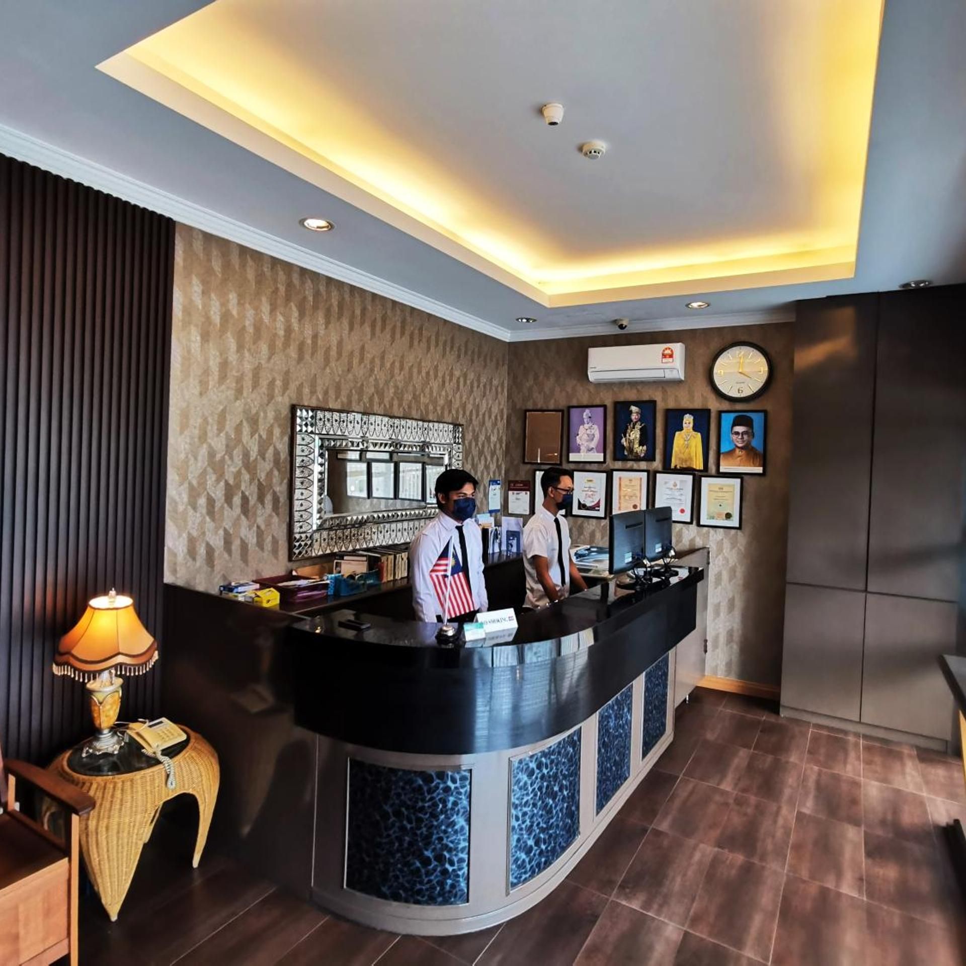 A hotel reception area with a curved counter, a clock, framed certificates, and a wall-mounted air conditioning unit.