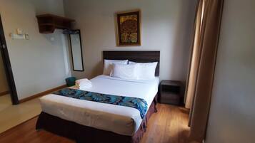 A hotel room with a large bed, a nightstand, a wooden floor, a wall-mounted shelf, and a painting.