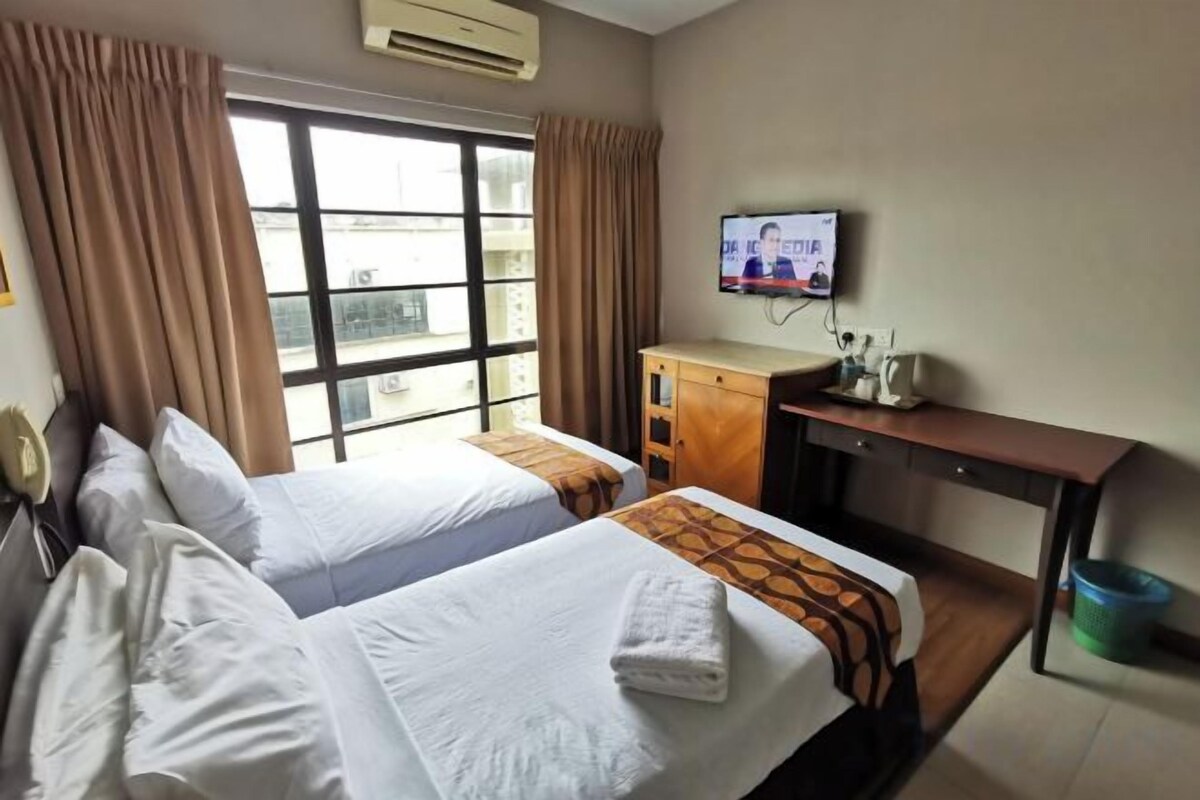 A hotel room with two beds, a television, a desk, and a window with curtains.