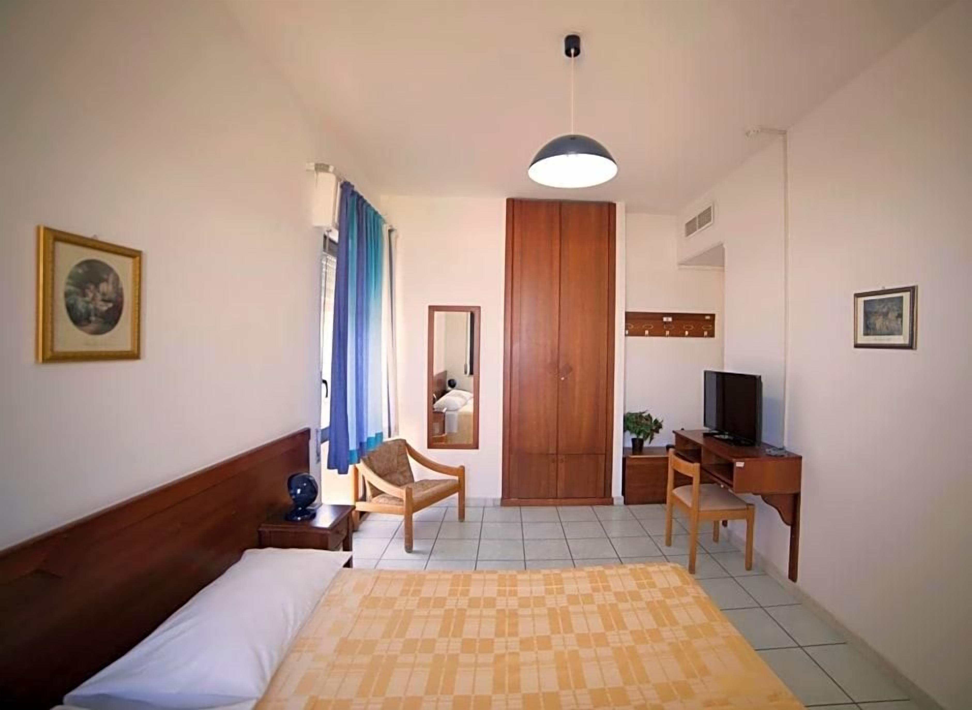 Ein Hotelzimmer mit einem Bett, einem Schreibtisch, einem Sessel, einem Fernseher und einem Kleiderschrank.
