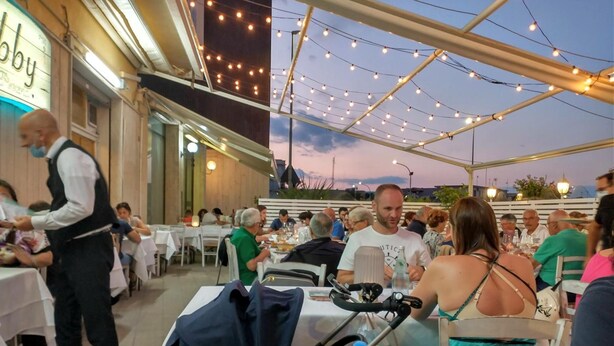 Un espace extérieur aménagé pour les repas, avec des guirlandes lumineuses, des tables et des convives.