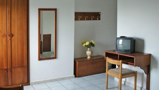 Une pièce comprenant une armoire en bois, un miroir, une petite table en bois avec un téléviseur et un vase rempli de fleurs.