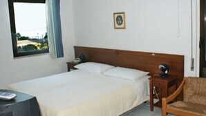 Une chambre d’hôtel avec un lit simple, une table de chevet, une chaise, une fenêtre donnant sur un paysage agréable et un tableau encadré au mur.