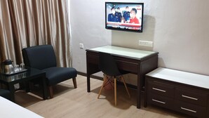 Habitación de hotel con escritorio, silla, televisor y una pequeña mesa con cafetera y vasos.