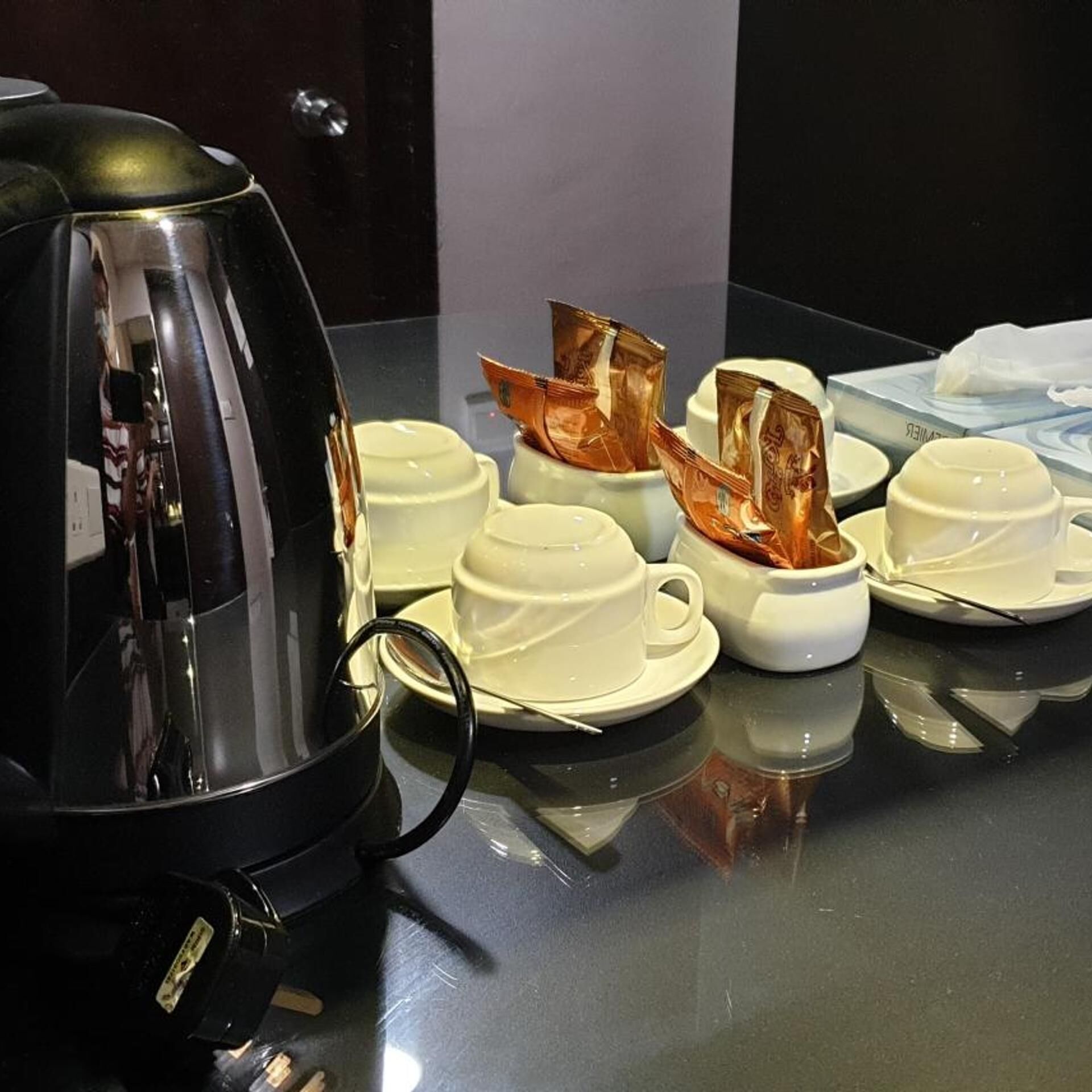 A coffee station with a black coffee pot, white cups, and a tissue box.