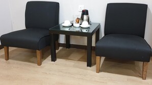 Dos sillas negras con patas de madera, una mesita de cristal con base negra y un enchufe blanco en la pared.