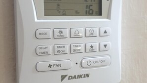 Un equipo de aire acondicionado Daikin blanco con pantalla digital, botones de control y el logotipo de la marca.