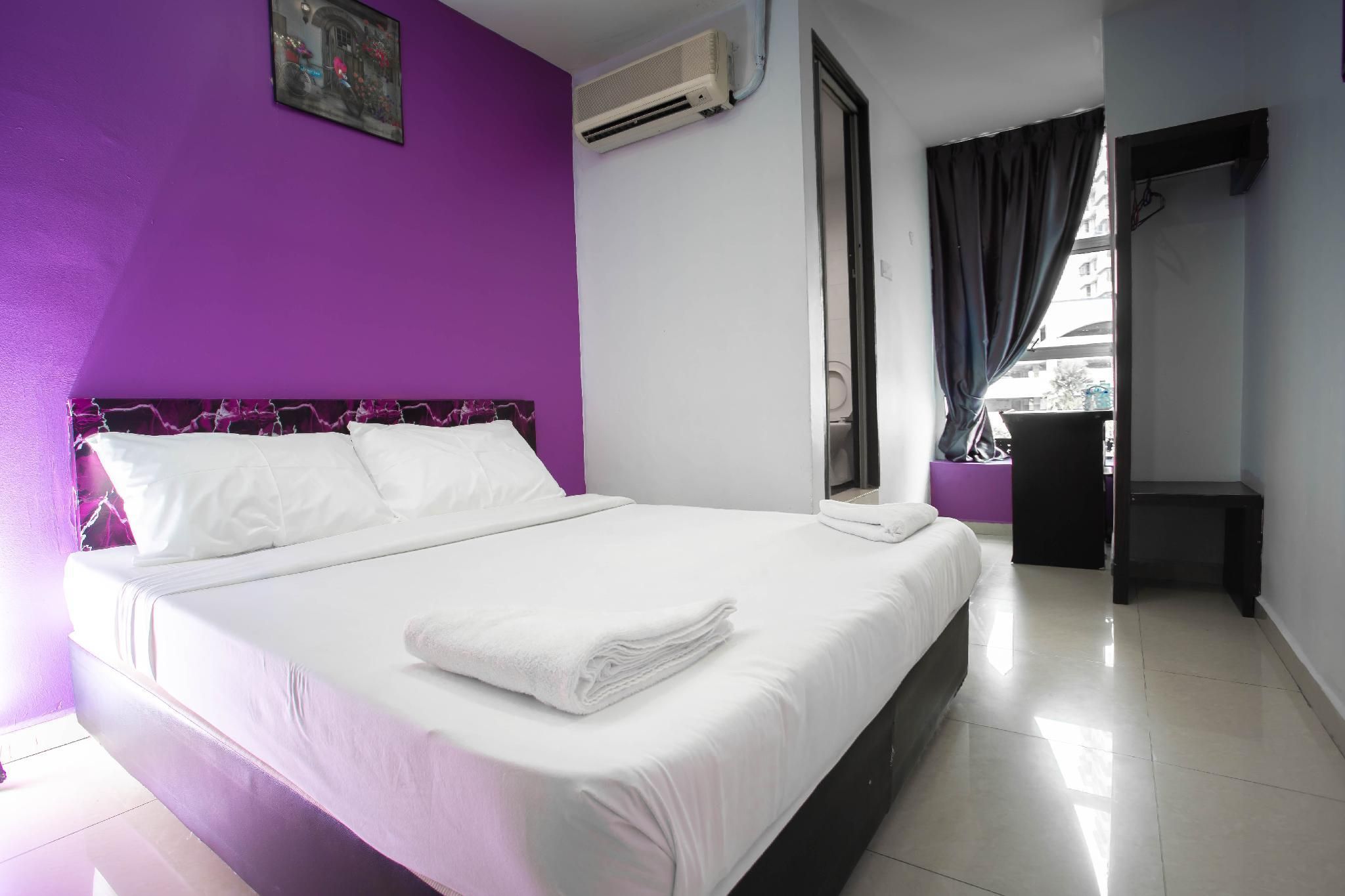A hotel room with a bed, a window with curtains, an air conditioning unit, and a door.