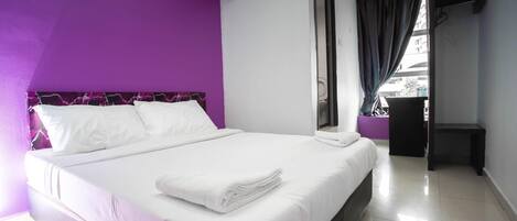 A hotel room with a bed, a window with curtains, an air conditioning unit, and a door.