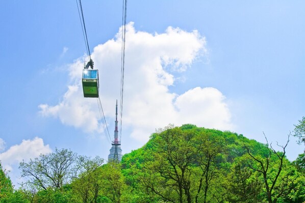 A cable car suspended between two towers, with a lush green hill and a clear sky in the background. - Nine Star Hotel Sinchon (Seoul)