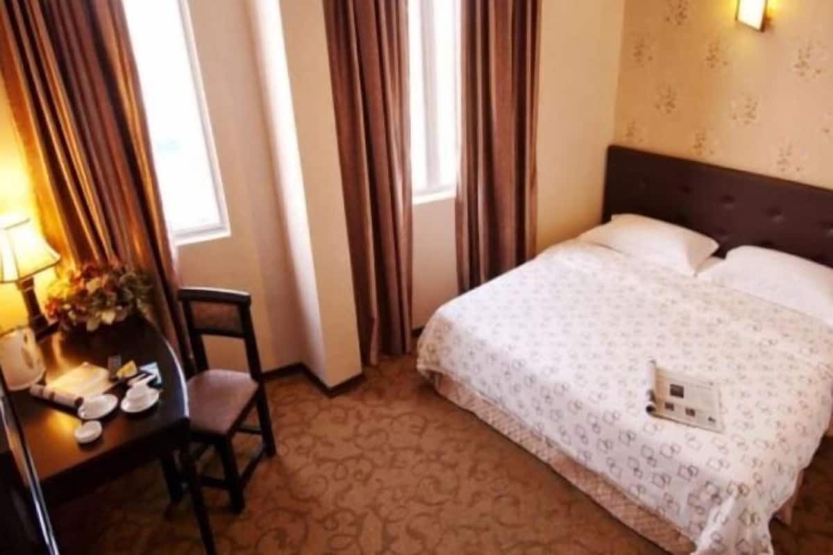 A hotel room with a bed, a desk with a lamp, and curtains.