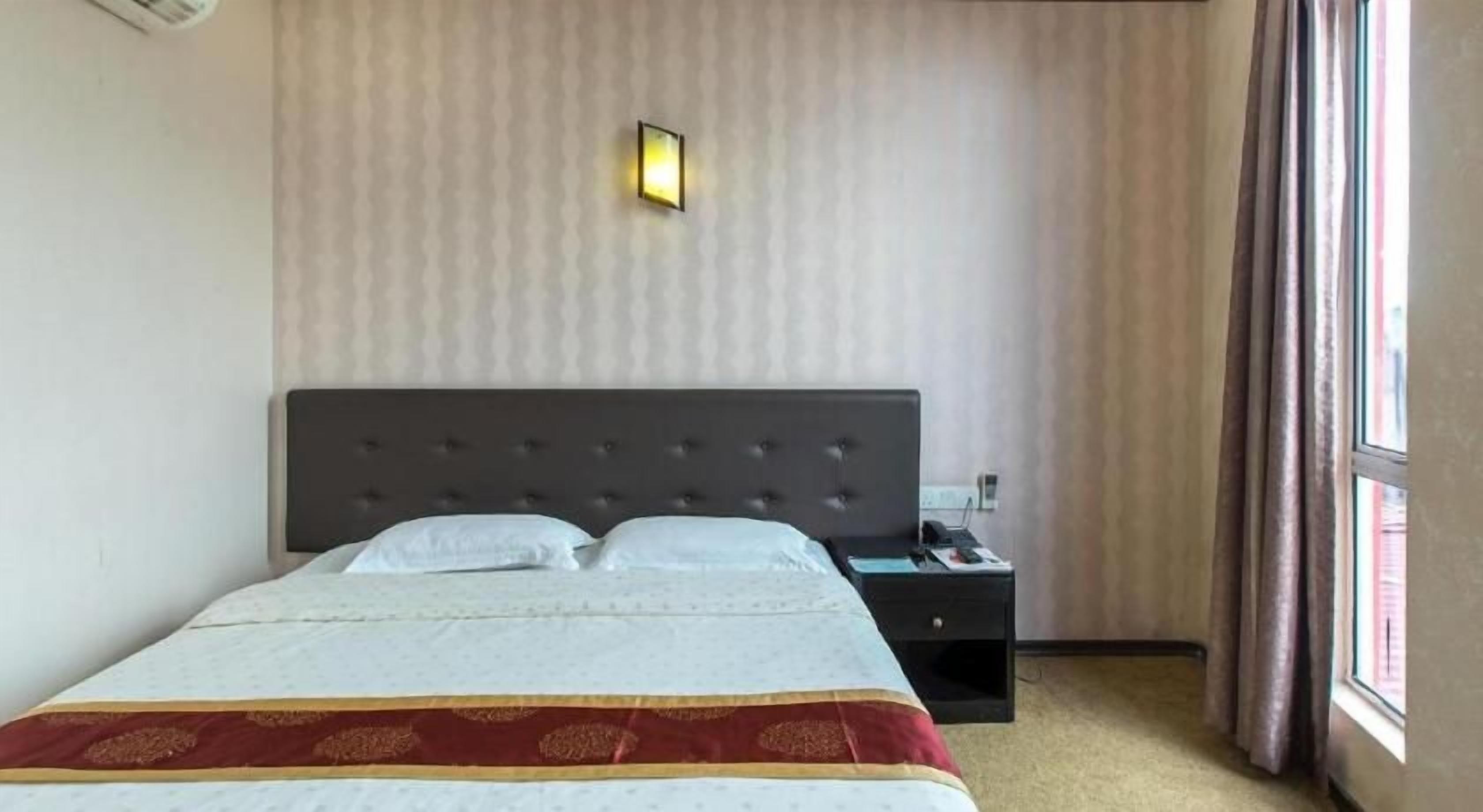 A hotel room with a bed, a nightstand, a wall-mounted light, and a window with curtains.