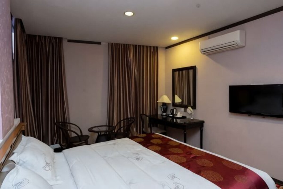 A hotel room with a bed, a desk with a lamp, a chair, a TV, and curtains.