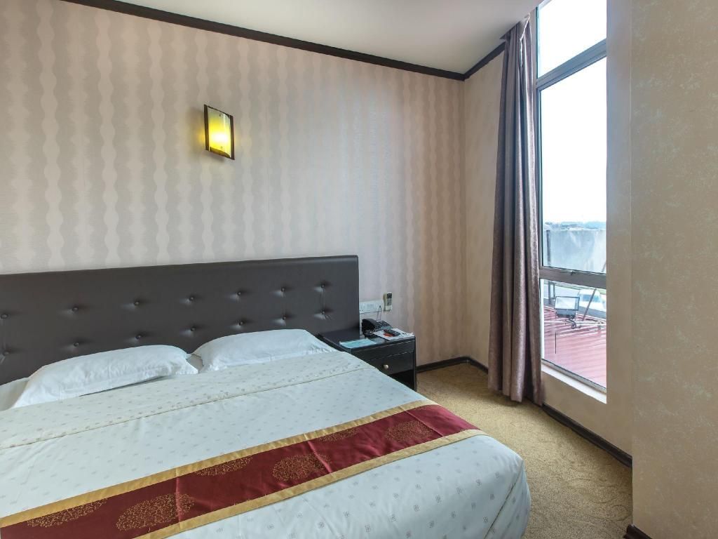 A hotel room with a large bed, a nightstand, a wall-mounted light, and a window with curtains.