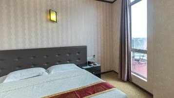 A hotel room with a large bed, a nightstand, a wall-mounted light, and a window with curtains.