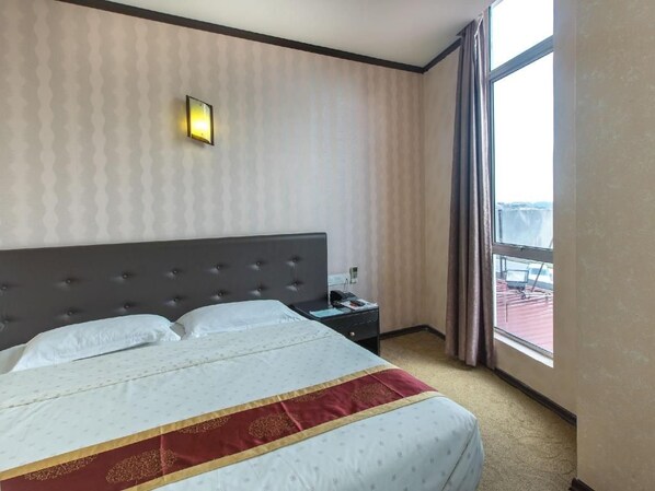 A hotel room with a large bed, a nightstand, a wall-mounted light, and a window with curtains. - S Bee Hotel (Johor Bahru)