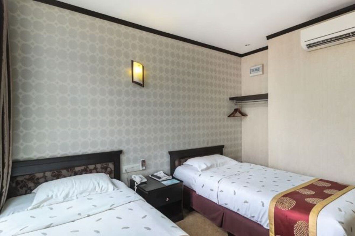 A hotel room with two beds, a nightstand, a wall-mounted phone, and a light fixture.