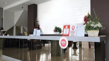 A reception desk with a sign indicating a location, a potted plant, and a wall-mounted sign.