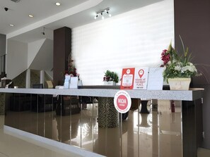 A reception desk with a sign indicating a location, a potted plant, and a wall-mounted sign. - S Bee Hotel (Johor Bahru)