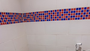 A standard white toilet with a closed lid, a showerhead, and a tiled wall with a red and blue mosaic border. - OYO 89891 1st Inn Hotel Subang (Subang Jaya)